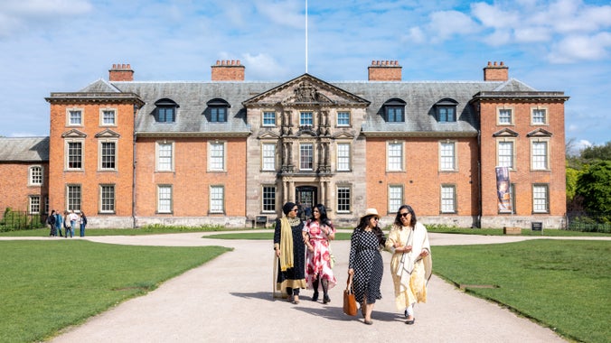 A group of visitors walking around Dunham Massey house on a sunny day.